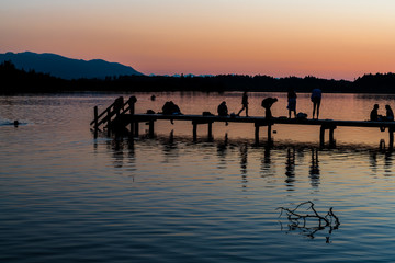 Kirchsee bei Bad T&ouml;lz mitHolzesteg, Badeg&auml;sten und Alpenblick nach Sonnenuntergang