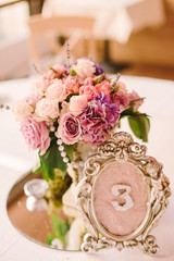 Table setting at wedding reception. Wedding floral decoration and stylized table number on guest table.