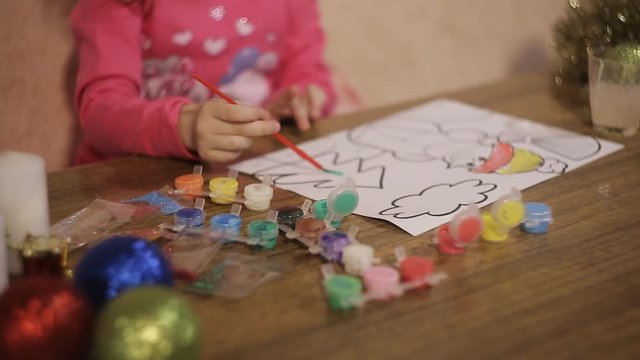 little girl diligently draws paints a Christmas picture winter evening