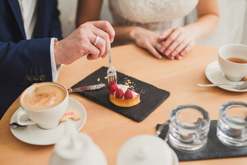 Closeup of bride and groom eating a sweet snack in cafe. Wedding rings on their fingers.