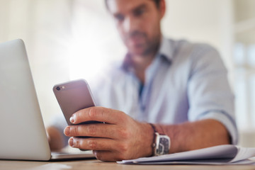 Young man using mobile phone while working on laptop