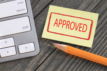 approved stamp on a note, with desk background