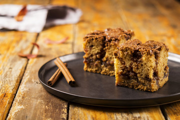 Cinnamon zucchini coffee cake on a black plate on a worn wooden light background with red dry leaves. Selective focus 