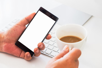 Mobil payment or digital banking concept. Hand holding smart phone with blank screen and cup of coffee on the working desk.