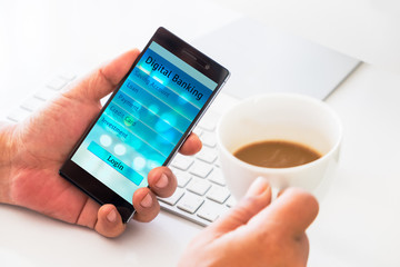 Mobil payment or digital banking concept. Hand holding smart phone with Digital banking application on screen and cup of coffee on the working desk.