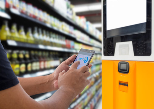 Mobile payment, Cashless society concept. Man using smart phone with NFC tag on screen in front of NFC money top up machine in supermarket.