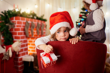 Cute little girl in the hat of Santa Claus with a gift in hand l
