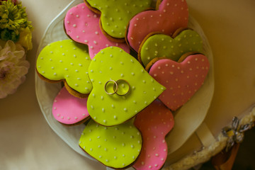 Green and pink cookie hears lie on the table with wedding rings