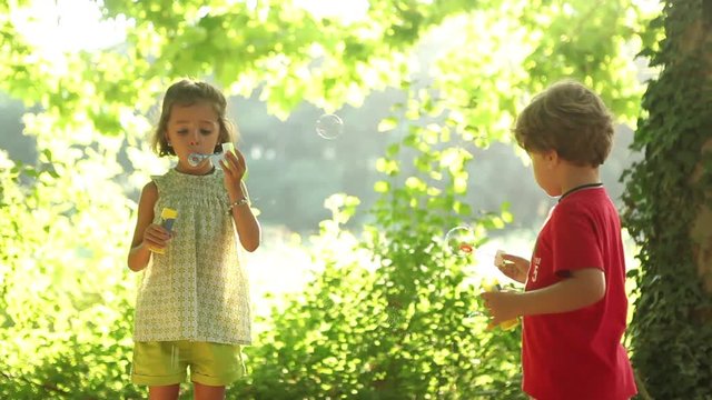 Young Boy and girl blowing soap bubbles outdoors holidays break happy enjoying life 