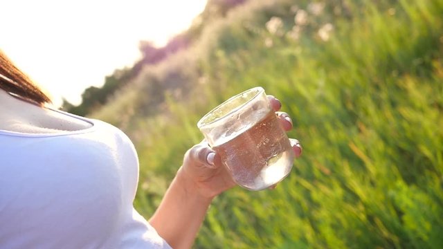 Woman hold a glass with clean pure water on nature green sunset background