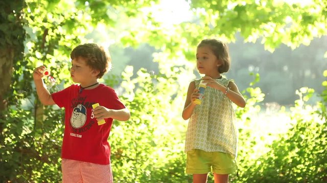 Young Boy and girl blowing soap bubbles outdoors holidays break happy enjoying life 