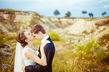 Radiant bride kisses groom's forehead while they stand on sand