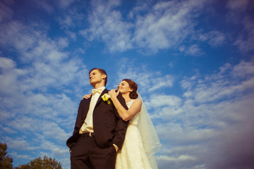 Bride and groom smile while standing under white clouds