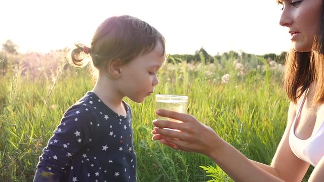 Mother gives child daughter drink clean pure water on sunset nature