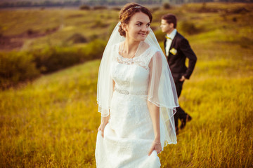 Fototapeta na wymiar Delicate veil covers bride's shoulders while she walks on the fi