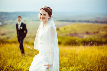 Attractive bride smiles light while standing on the filed before