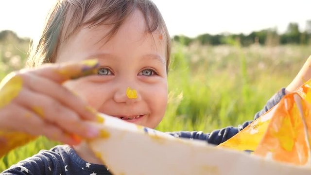 Portrait of cute happy little child girl play on sunset nature meadow with just painted paper ship
