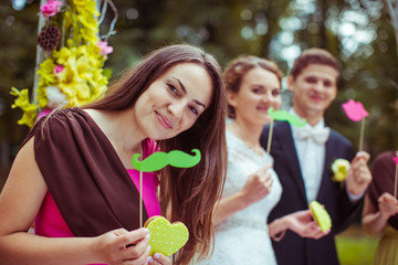 Bridesmaid in pink dress holds green paper moustache