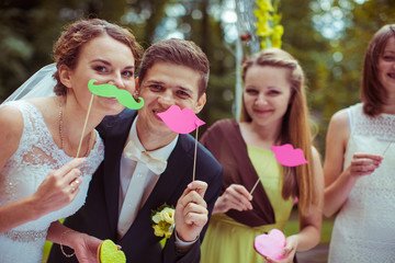 Bride, groom and friends hold paper moustaches before their face