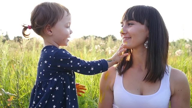 Child painting her mother face and kiss having fun on nature sunset