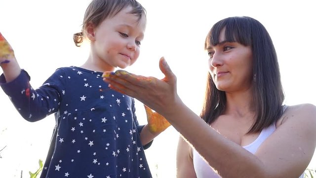 Young mother and little daughter high five with colored painter hands during nature meadow walking