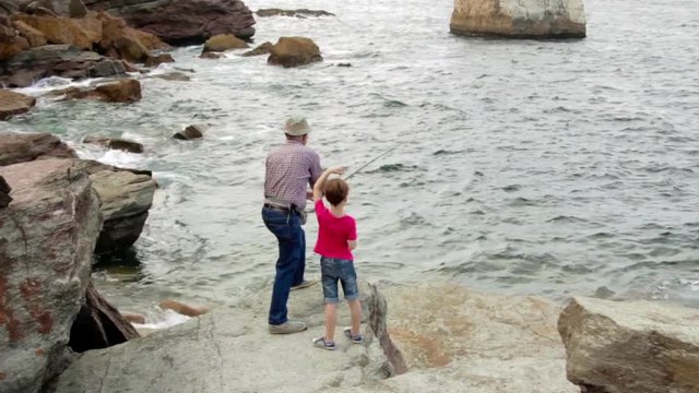 Senior man with child throwing fishing rod to the sea