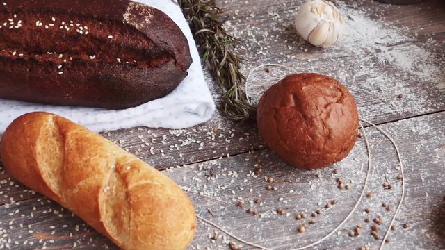 Different types of bread on wooden table dusted with flour. Slow pan.