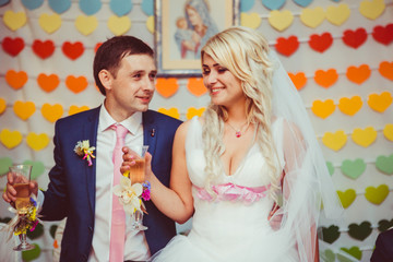 Happy newlyweds stand before a wall with colorful paper hearts