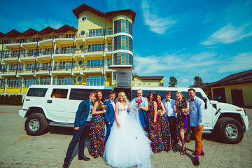Newlyweds and their stylish band stand before a white limousine