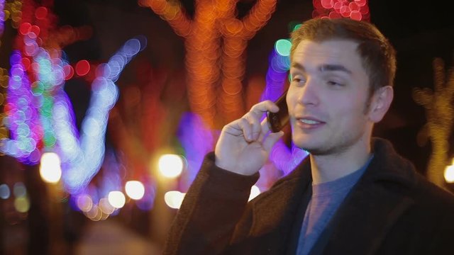 The young man smiles and speaks by phone with someone