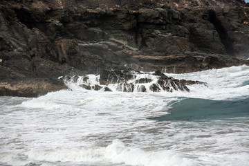 Wave splashing over a rock on the beach of Puertito de los Molinos on Fuerteventura. Canary Island, Spain