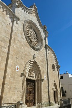 Ostuni cathedral façade in Ostuni, Italy. Facade with its signature rose window, set against a cloudless blue sky
