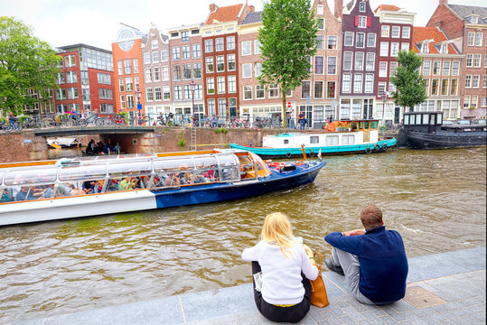 Tourists admire the canals of Amsterdam and features buildings