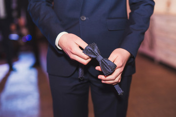 Fototapeta premium Caucasian guy in suit holding bow tie in his hands