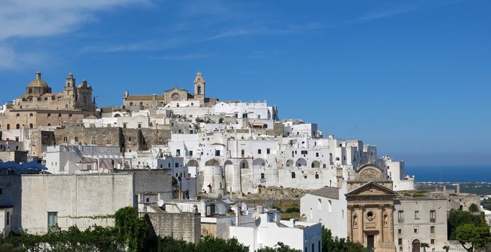 Ostuni, Italy, "the White City," on a hilltop in Apulia, Italy beneath blue sky. Adriatic Sea is visible in the distance.