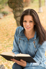 Fototapeta premium Beautiful young woman reading a book in park at fall