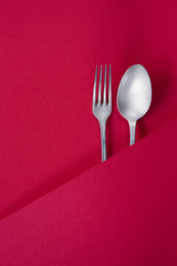 Ancient silver fork and spoon on red background. Covered by red decorative paper with copy space on it