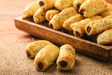 Puff pastry sausage rolls on brown wooden background.
