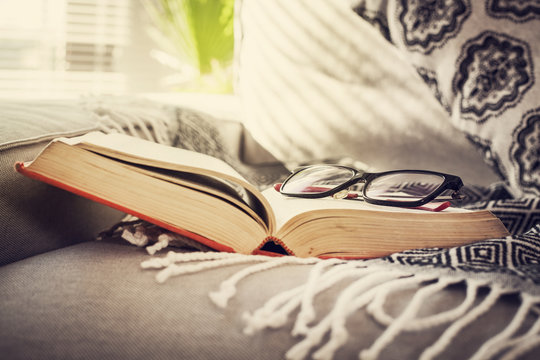 Reading book with eyeglasses on sofa