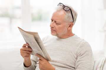 senior man in glasses reading newspaper at home