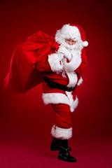 Santa Claus comes with a big bag of gifts. Full length portrait.
