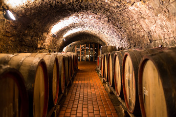 Fototapeta na wymiar Old wooden barrels with wine in a wine vault, aged traditional wooden vine barrels lined up in cool and dark vine cellar, Italy, Porto, Portugal, France