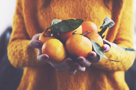 Woman in yellow knitted pullover with ripe clementines in her ha