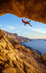 Deurstickers Male climber on overhanging rock against beautiful view of coast below  © Andrey Bandurenko