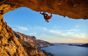Gardinen Male climber on overhanging rock against beautiful view of coast below © Andrey Bandurenko