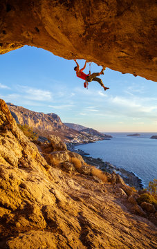 Male climber on overhanging rock against beautiful view of coast below 