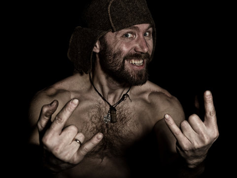 Dark portrait of scary evil sinister bearded man with smirk, shows sign of heavy metal. strange Russian man with a naked torso and a woolen hat