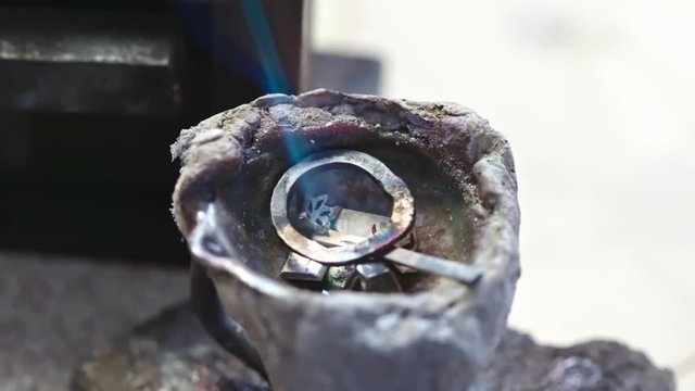 Zoom out of few jewelry things melting down by flame of torch during process of recasting them into new item