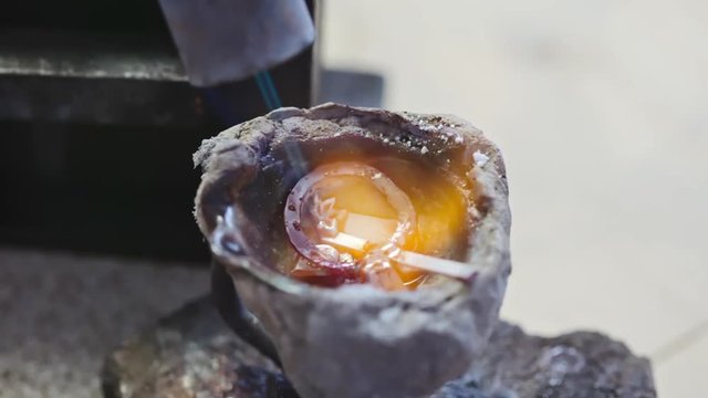 Closeup of jewelry in metal bowl melting down by flame of torch during process of recasting them into new item