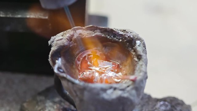 Zoom out of precious metal melting in bowl with gas torch for jewelry making